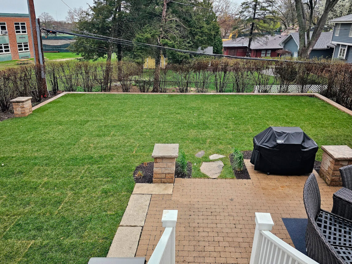 High-angle view of a freshly restored green lawn and paver patio with stone pillars after a backyard pool removal project in Winnetka.