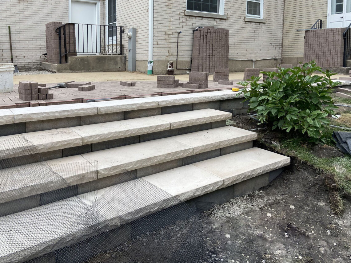 In-progress construction of light-colored stone stairs and retaining wall steps leading to a prepped paver patio area in a Wilmette backyard.