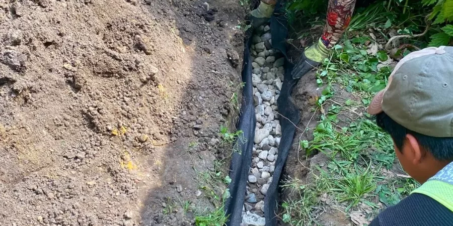 Worker installing a French drain system as part of fall drainage maintenance in a Glenview yard to prevent subsurface water pooling and protect the foundation.