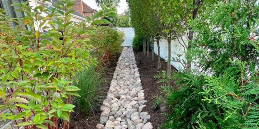 Glencoe backyard featuring river rock swale and underground flow wells redirecting water and preventing yard flooding.