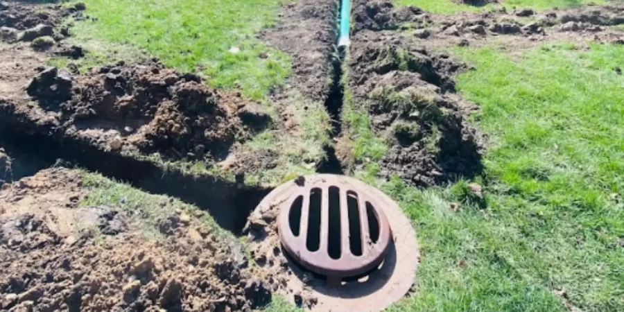 French drain vs. channel drain trench in Glenview lawn showing exposed pipe and round curb basin.
