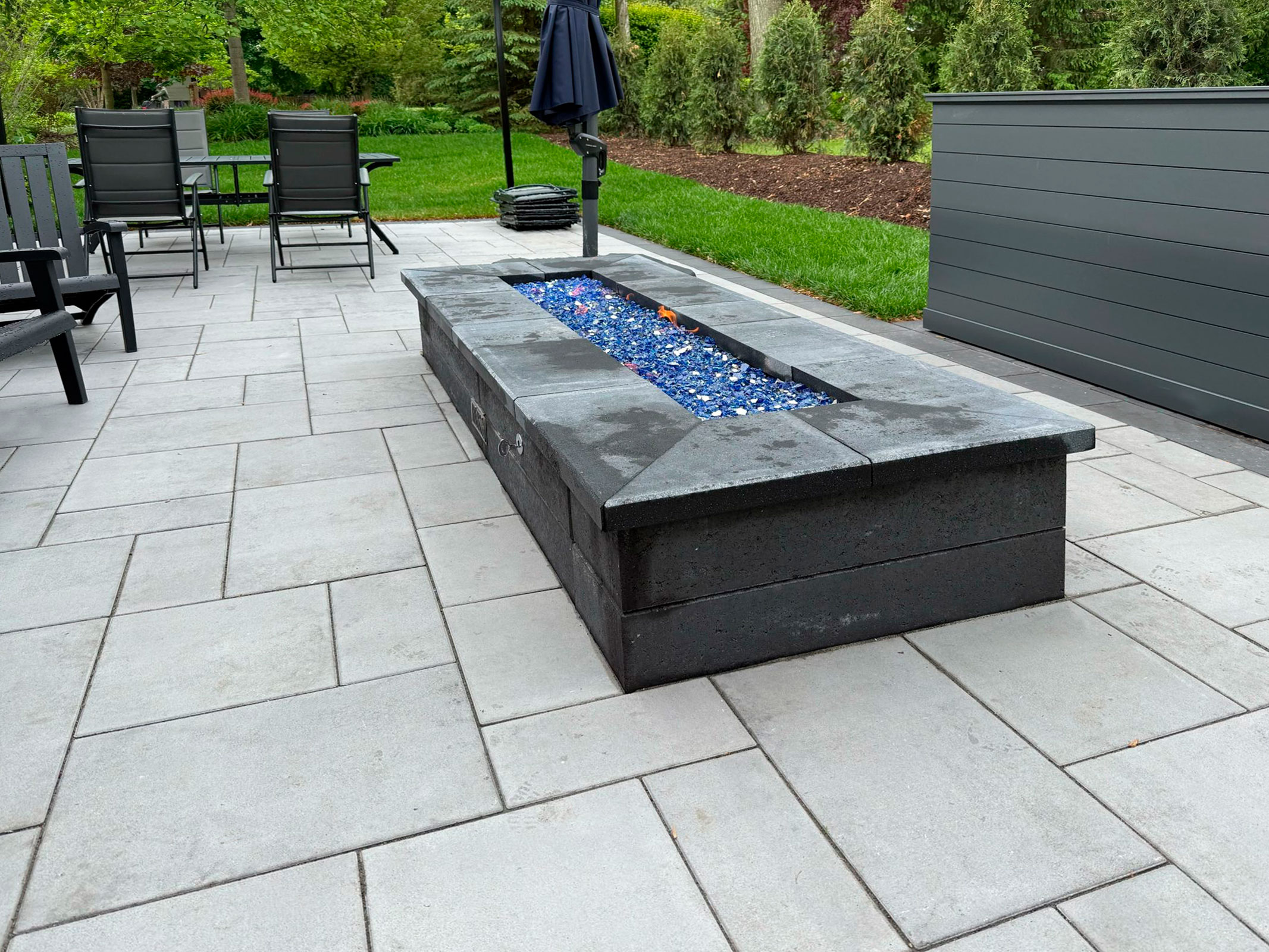 Modern patio hardscape installation with sleek stone pavers and a built-in rectangular fire pit centerpiece.