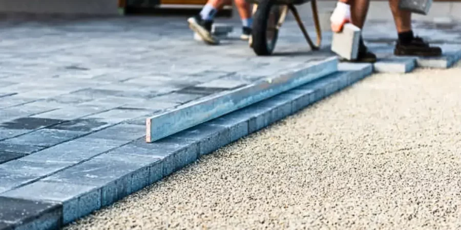 Workers installing pavers on a compacted gravel base, ensuring stable hardscaping solutions for outdoor spaces.