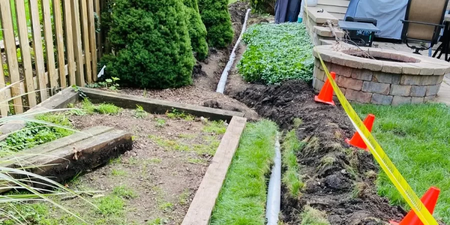 Landscape drainage solutions with underground pipe installation to redirect yard water away from patio and garden.